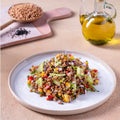 A delicious buckwheat salad served on a white plate, garnished with cucumbers, peppers, and herbs, paired with a bottle of olive oil and whole buckwheat grains in a wooden spoon.