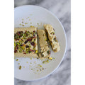 Slice of pistachio halva on a white plate, with additional pieces beside it, highlighting the ingredients and texture of the confection.