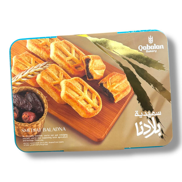 Qabalan Premium SMEDIAH packaging showcasing traditional Arabic desserts. The image features an assortment of delicious stuffed pastries arranged on a wooden serving board with dates and wheat, highlighting their rich texture and flavor.
