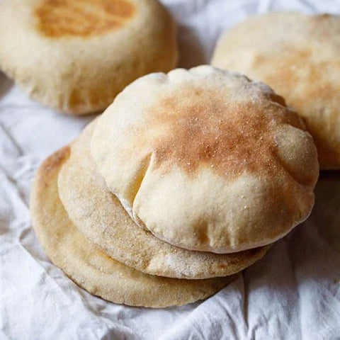 Close-up of four pieces of Albasha Fresh Baked Pita Bread - 10 Pieces of Soft, Chewy, highlighting the golden-brown surface and inviting softness ideal for dipping and stuffing.