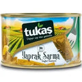 Tukaş stuffed vine leaves in a can, featuring a picturesque countryside background and the brand logo prominently displayed. The label reads 'Yaprak Sarma' indicating the product type.