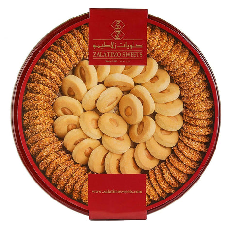 A beautifully arranged round tin of Zalatimo Sweets featuring an assortment of sesame cookies and butter cookies, showcasing a traditional Middle Eastern design. The tin is red with a gold logo and is filled with cookies with a crispy texture and visible nuts. Ideal for gifting or sharing during special occasions.